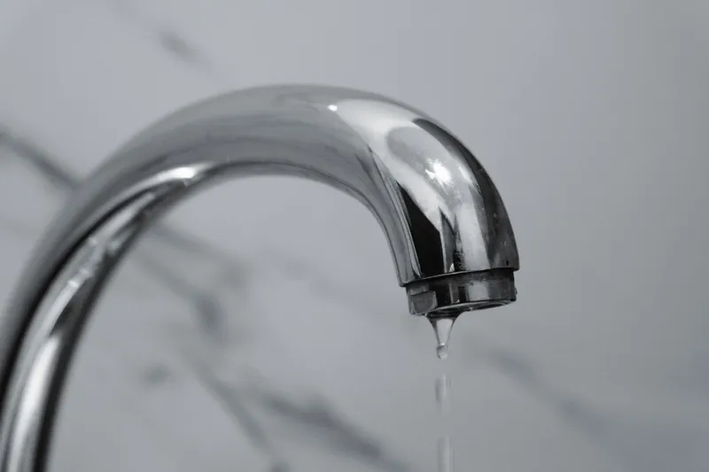 Rubinetto cromato da cui scende una goccia d'acqua